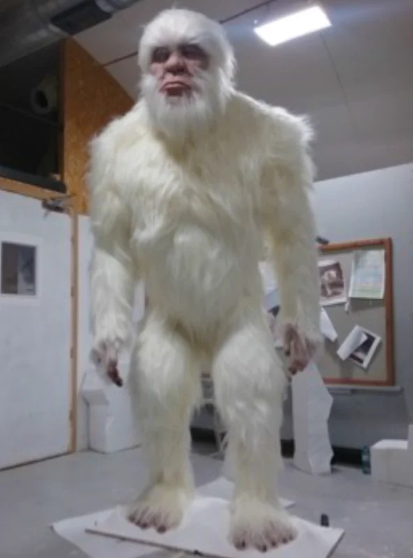 Large, lifelike yeti sculpture with long white fur, standing in a workshop or studio space.